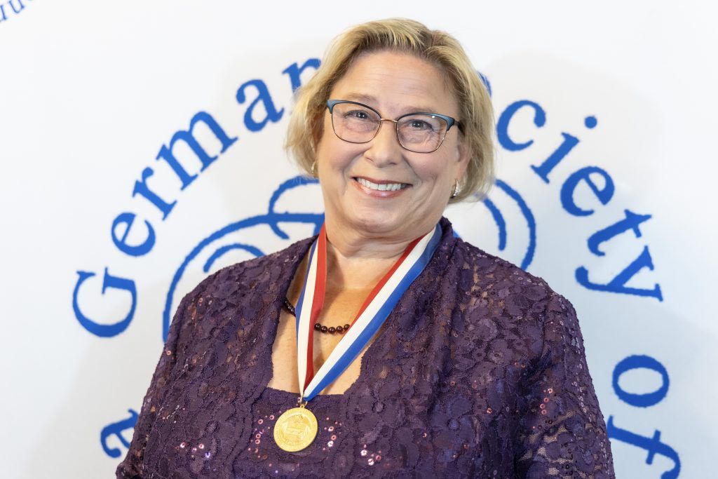 Woman wearing a medal and purple jacket in front of a German Society backdrop