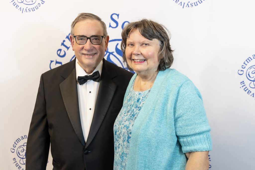 Two smiling people posing at a formal event, wearing a tuxedo and a light blue dress