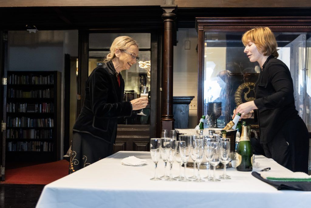 Two people standing at a table with wine glasses and bottles in a formal dining room