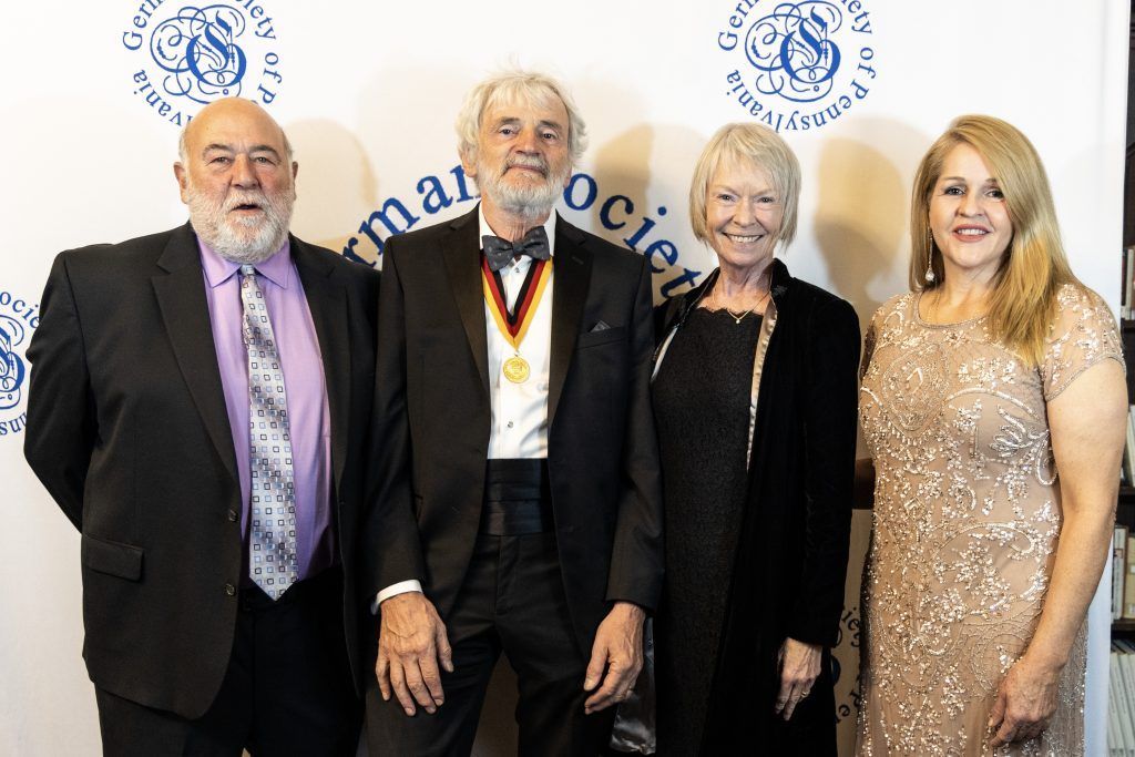 Four formally dressed people posing at an awards event in front of a branded backdrop.