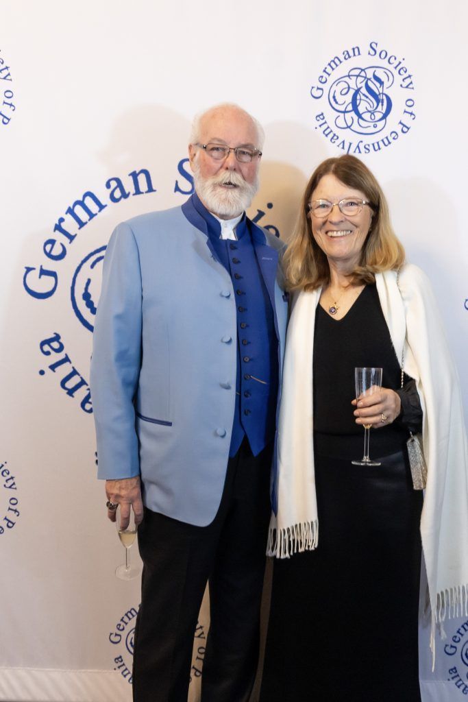 Two people posing at a German society event backdrop, smiling and holding a wine glass