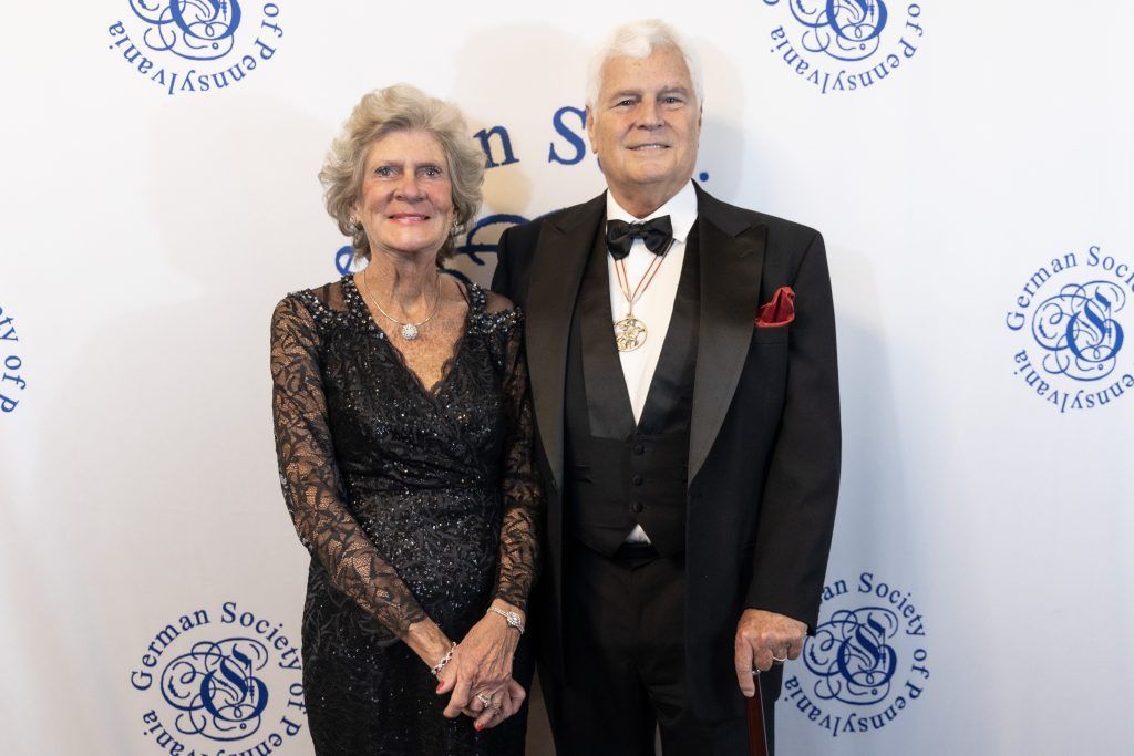Two people posing at a formal event in black attire before a white step-and-repeat backdrop