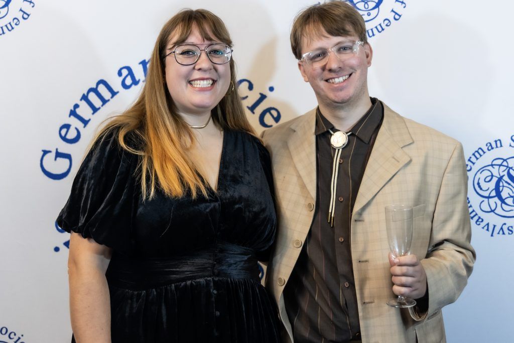 Two people posing at a formal event backdrop, smiling in dressy outfits.