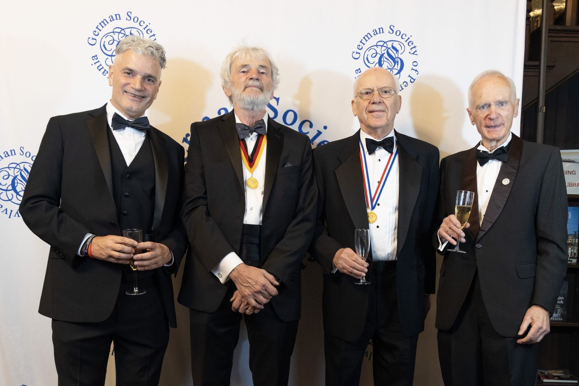 Four men in suits holding drinks pose at a formal awards event