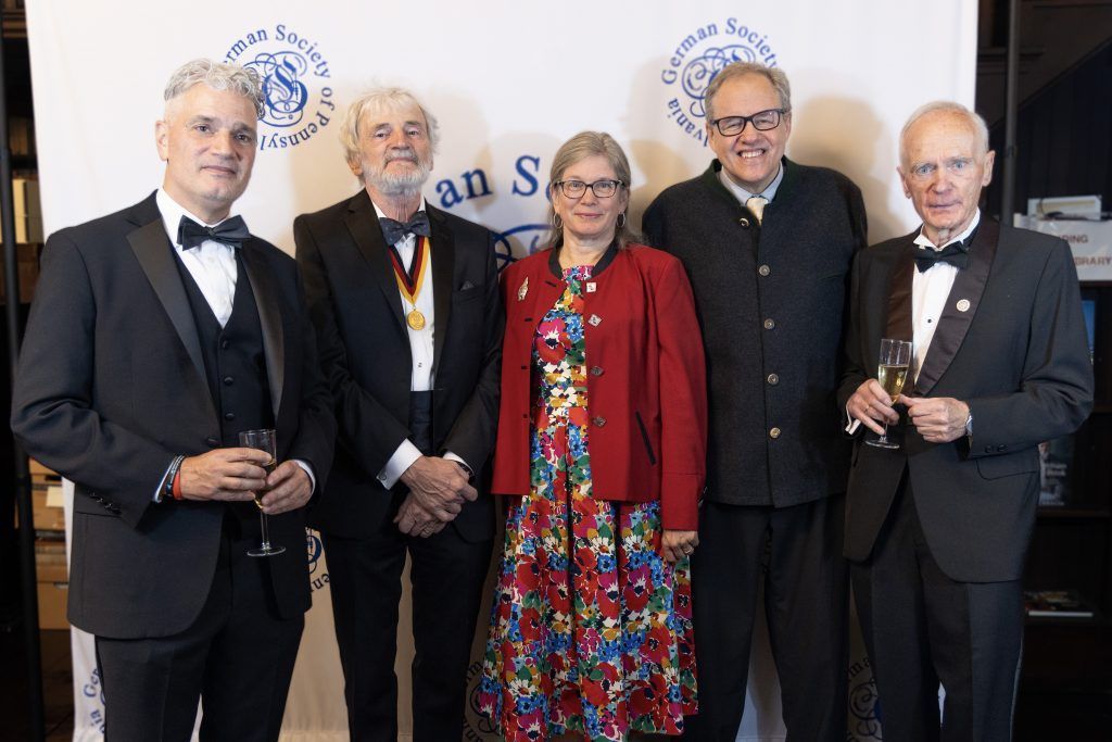 Five people in formal attire posing together at an awards event backdrop