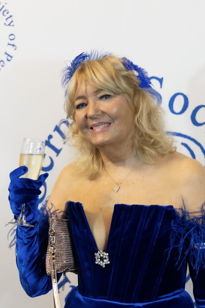 Woman in a royal blue strapless gown and gloves, smiling at a formal event backdrop