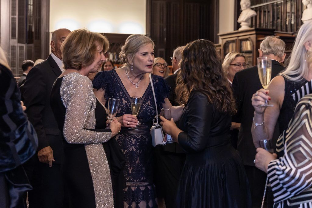 Guests in formal attire mingle and chat at an elegant indoor reception.