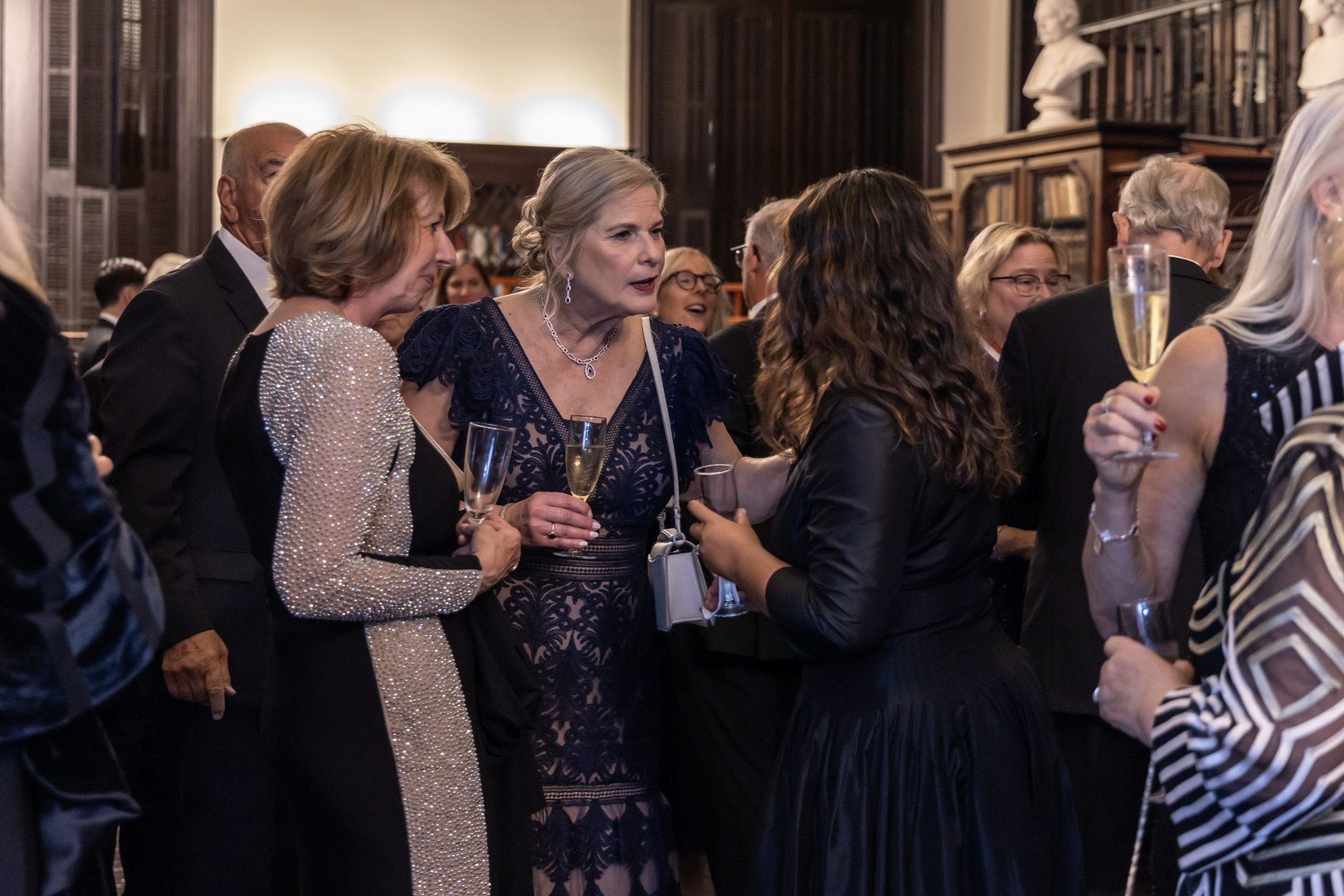 Guests in formal wear chatting and holding drinks at a lively indoor reception.