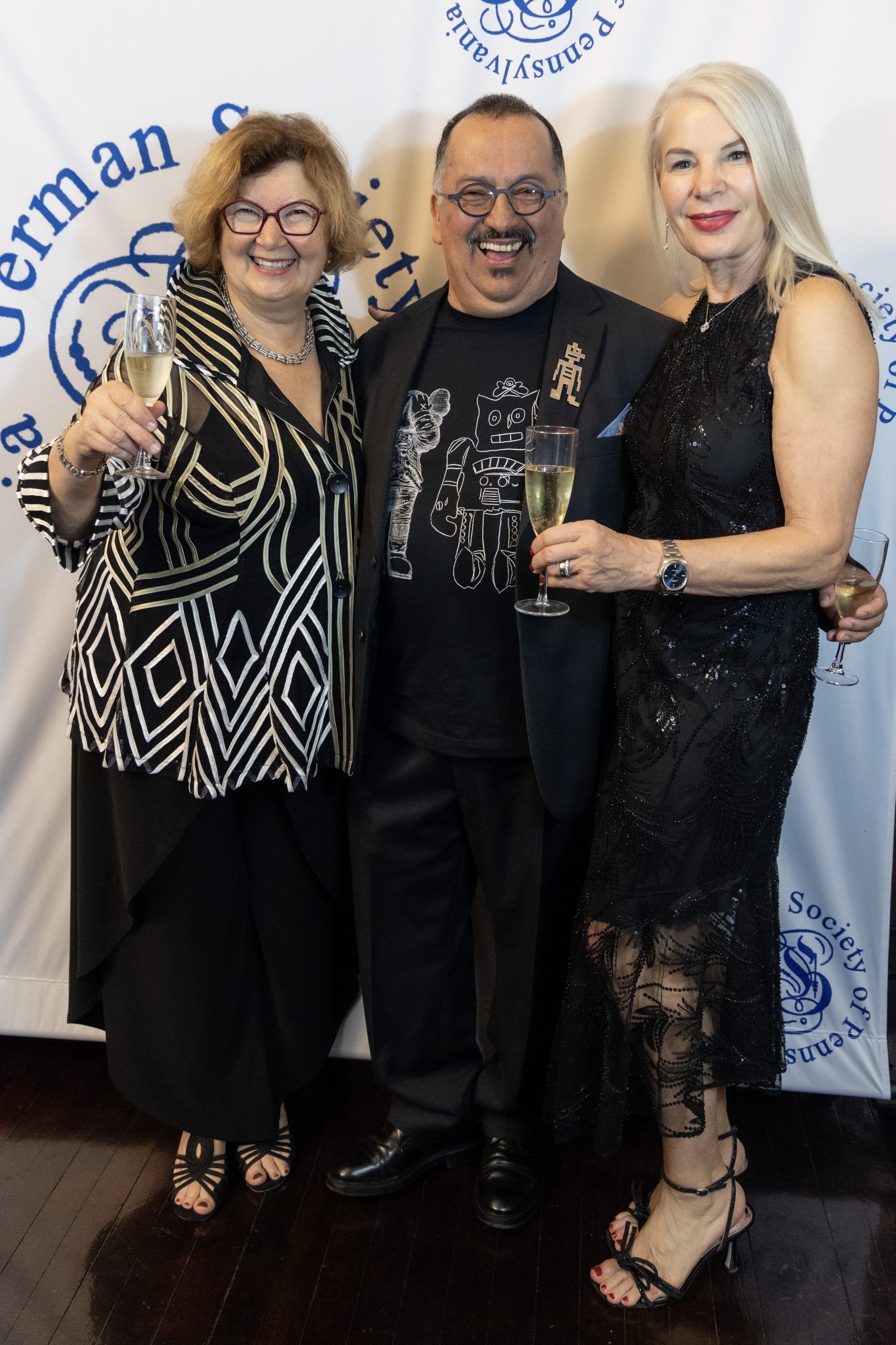 Three people posing together at a formal event backdrop, smiling in black outfits.
