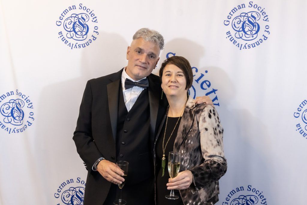 Two people posing at a formal event backdrop, smiling and holding drinks.