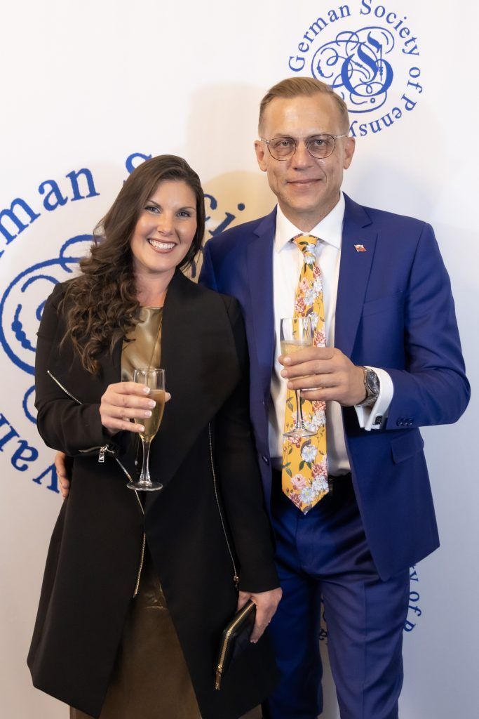 Two people in formal attire holding champagne flutes at a branded event backdrop