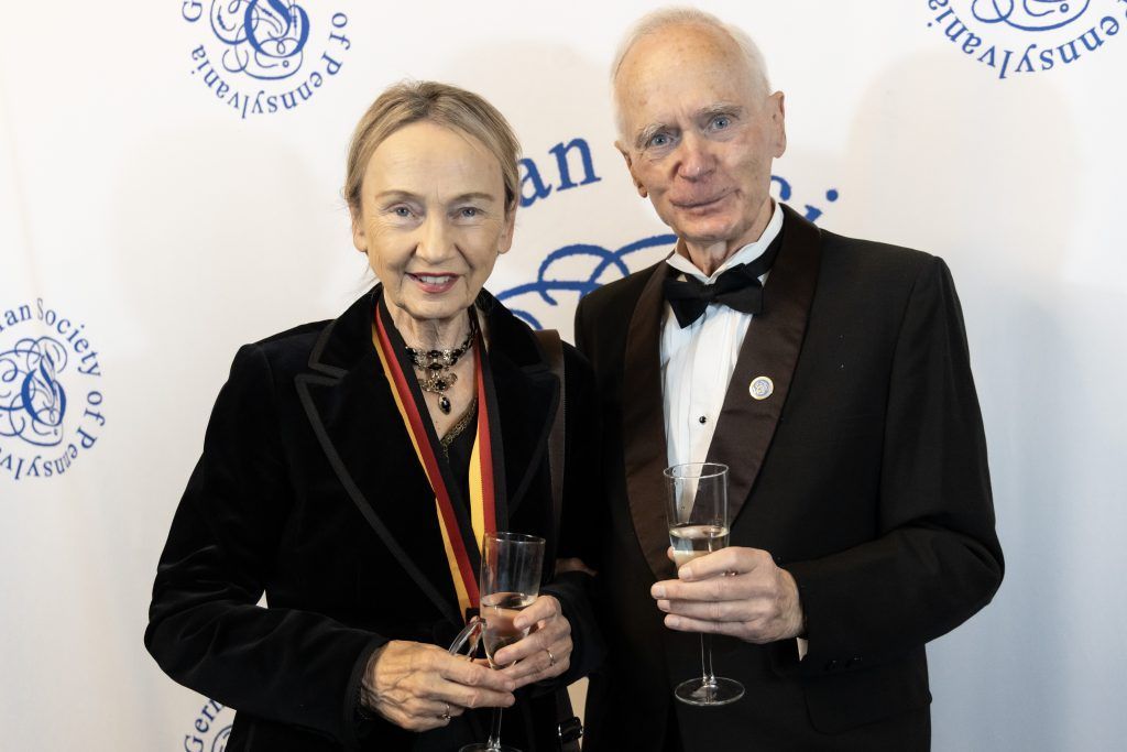 Two formally dressed people holding awards and glasses at a gala backdrop
