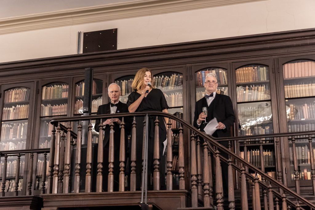 Three people on a wooden balcony in front of shelves of books and files