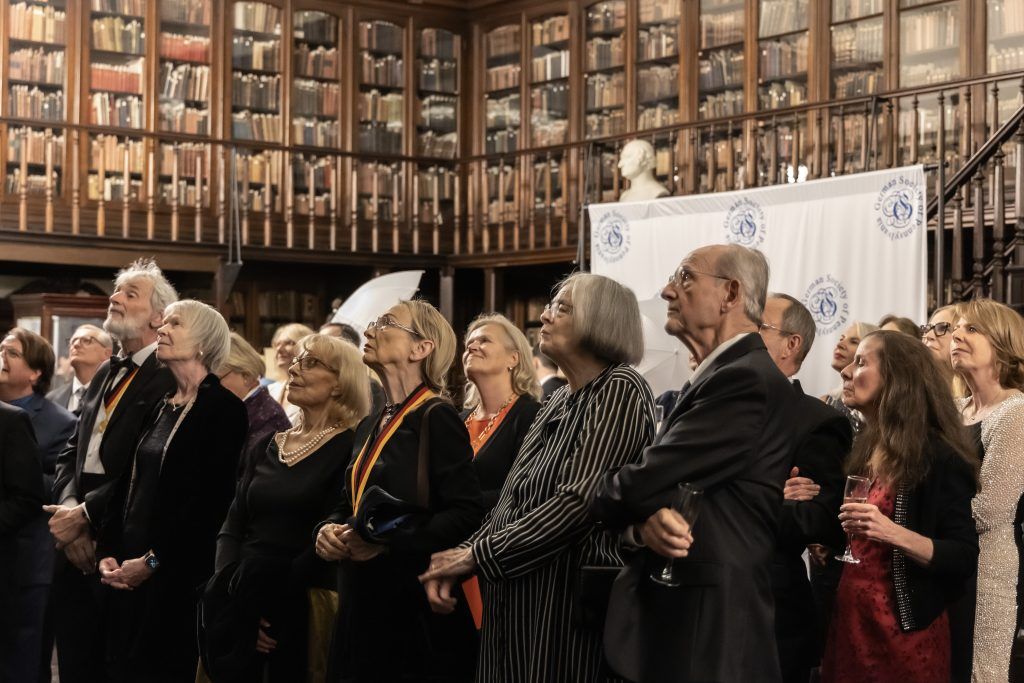 People standing closely together in a grand library hall, facing forward during an event