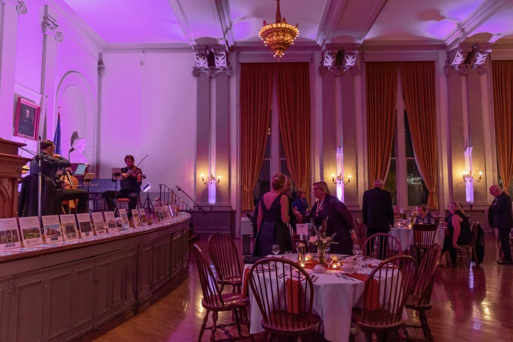 Elegant banquet hall with round tables, tall red curtains, chandeliers, and soft purple lighting during an event