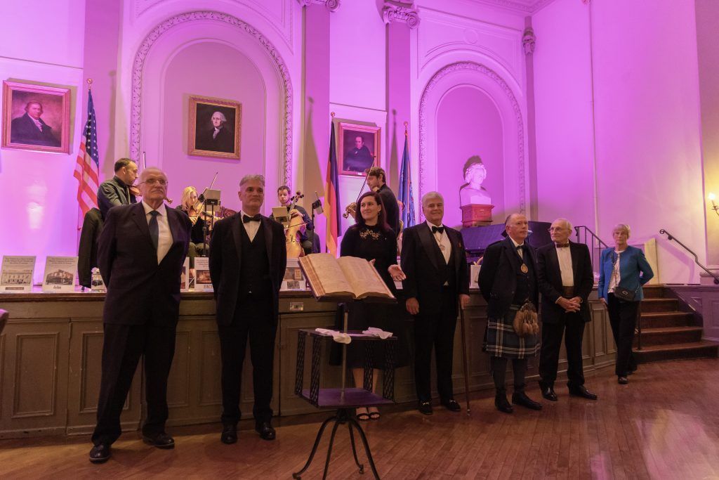 People standing in a grand hall with purple lighting, gathered near a counter and a staircase
