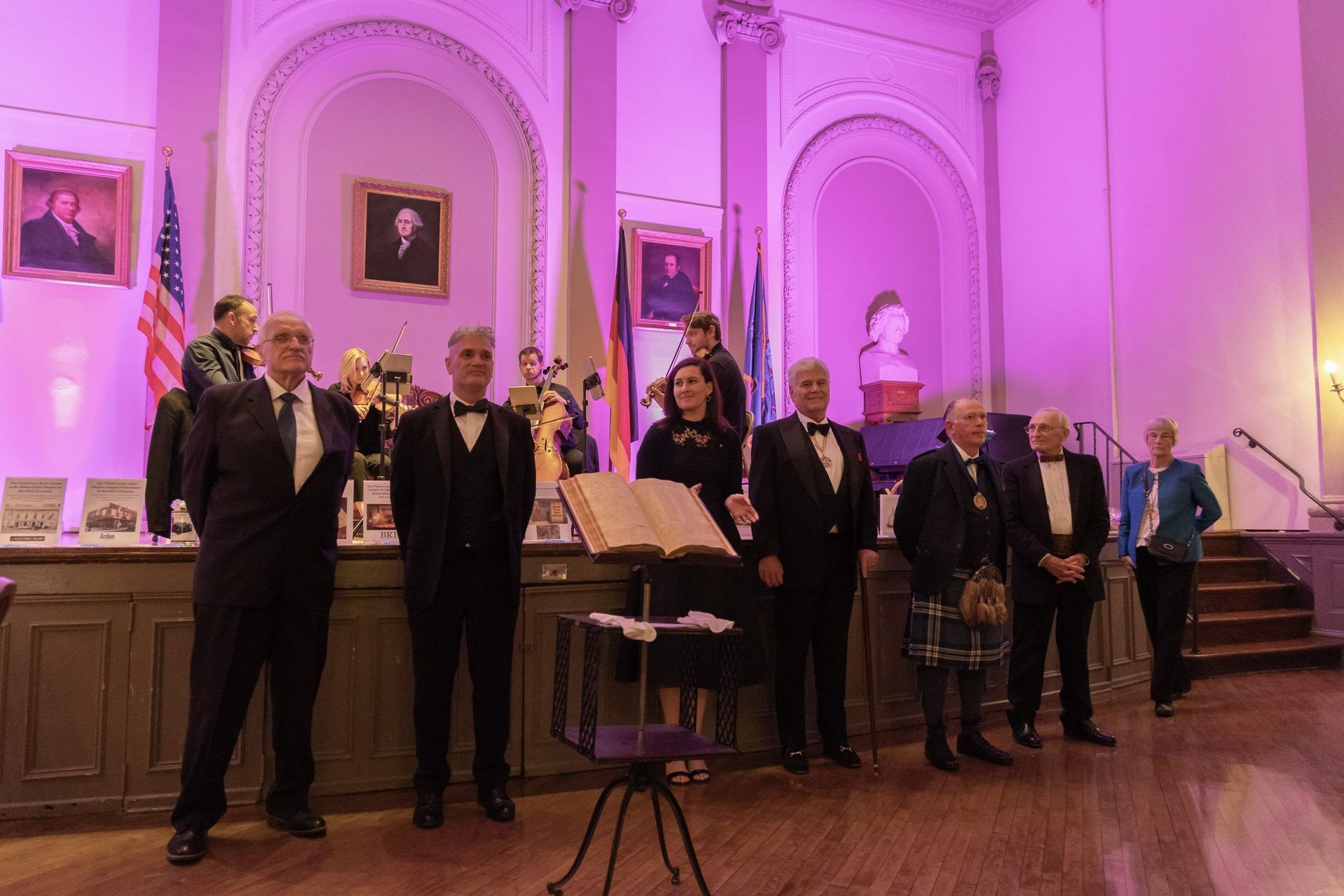 People standing in a purple-lit hall beside a lectern, posing for a group photo