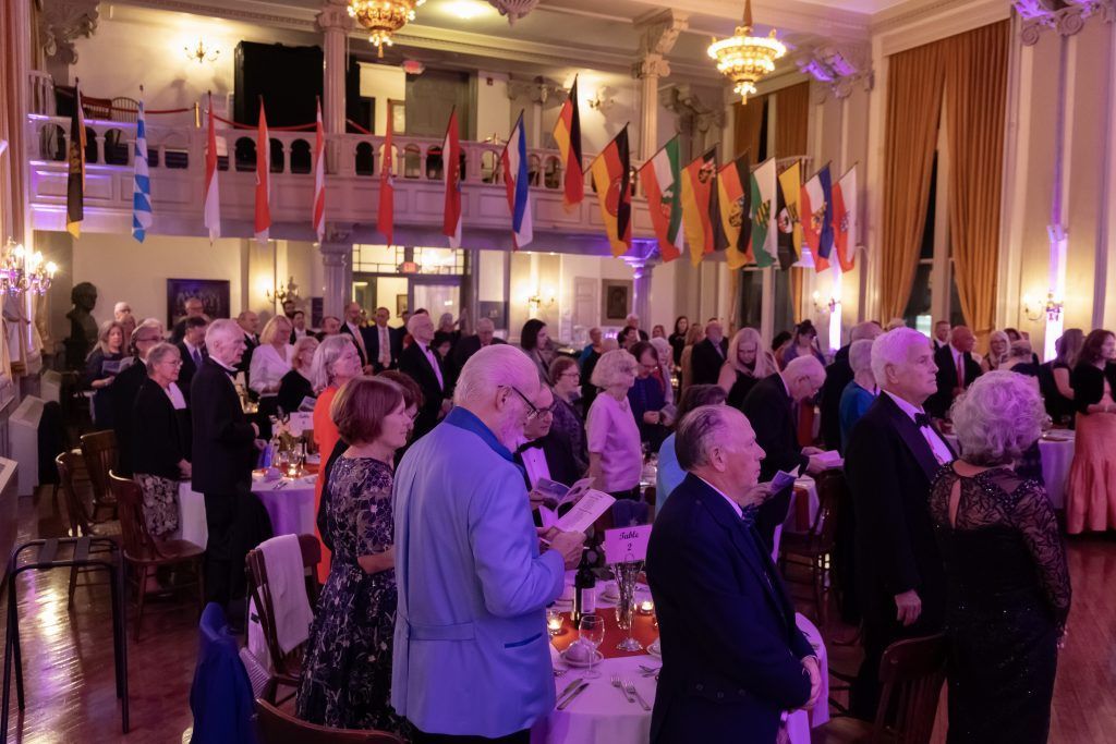 Crowded banquet hall with people mingling under colorful flags and chandeliers