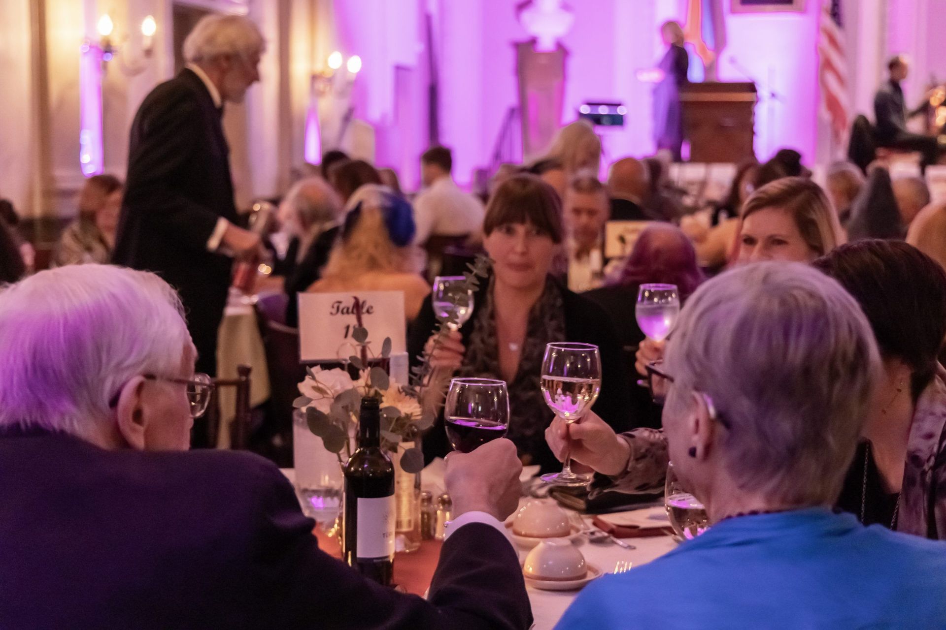 Guests dining at a banquet table in a softly lit ballroom with purple uplighting