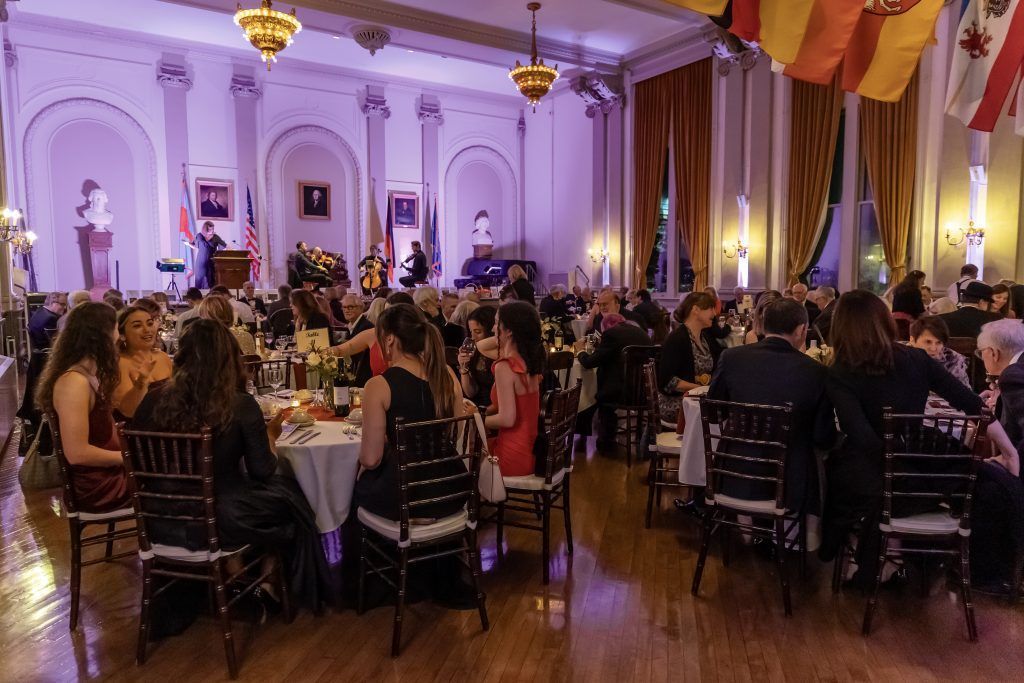 Guests seated at round tables in a grand banquet hall with chandeliers and purple lighting
