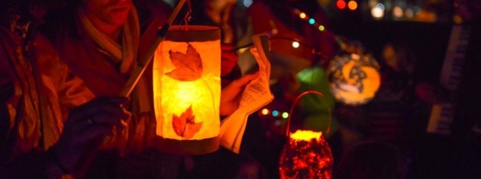 People holding glowing red lanterns at a nighttime celebration, with warm lights in the background
