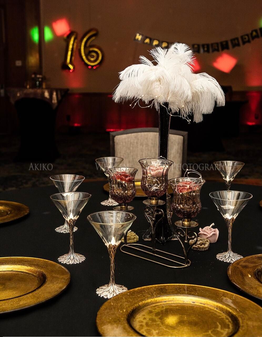 Table setting for a party with gold and black decor, martini glasses, and a centerpiece.