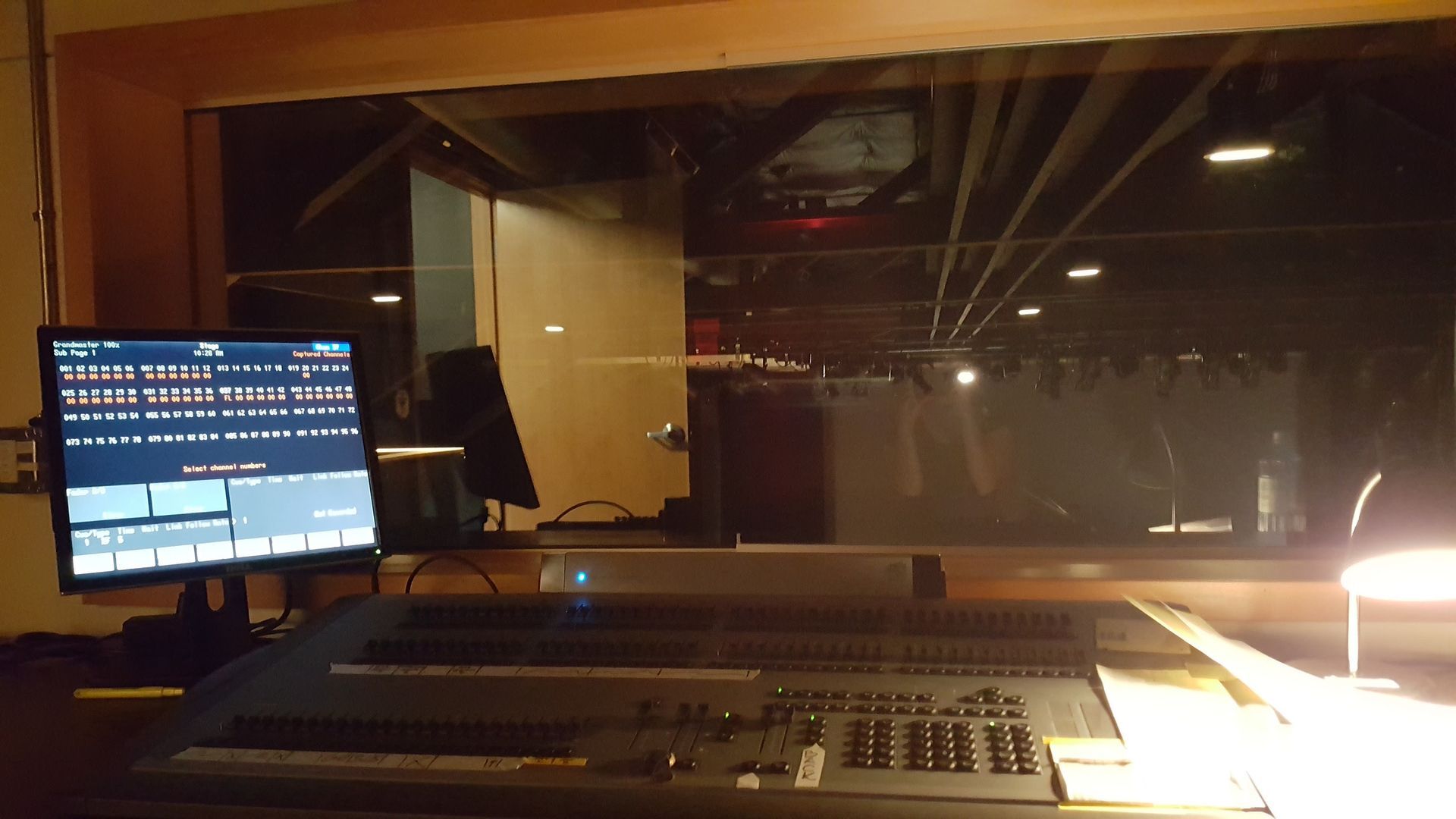 Control room overlooking a stage with a lighting console and computer monitor displaying controls.