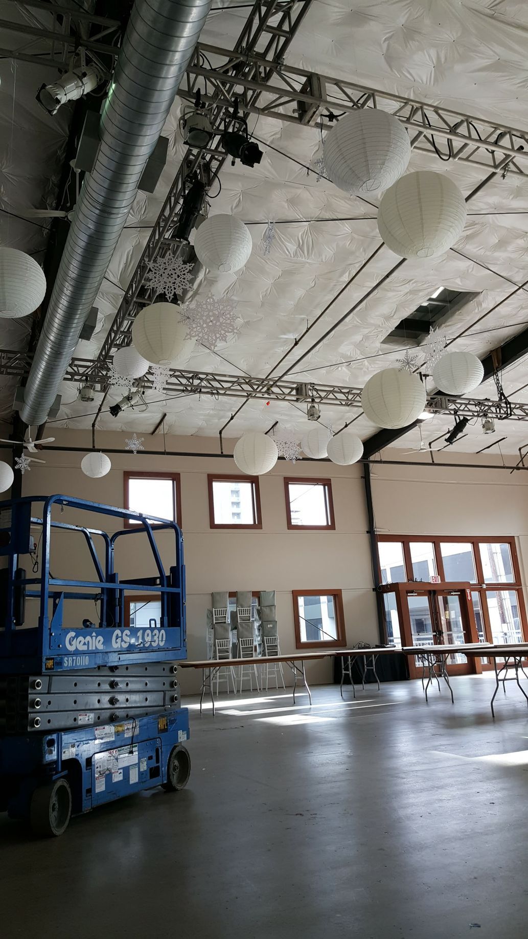 A blue scissor lift inside a large event space with white paper lanterns hanging from the ceiling.