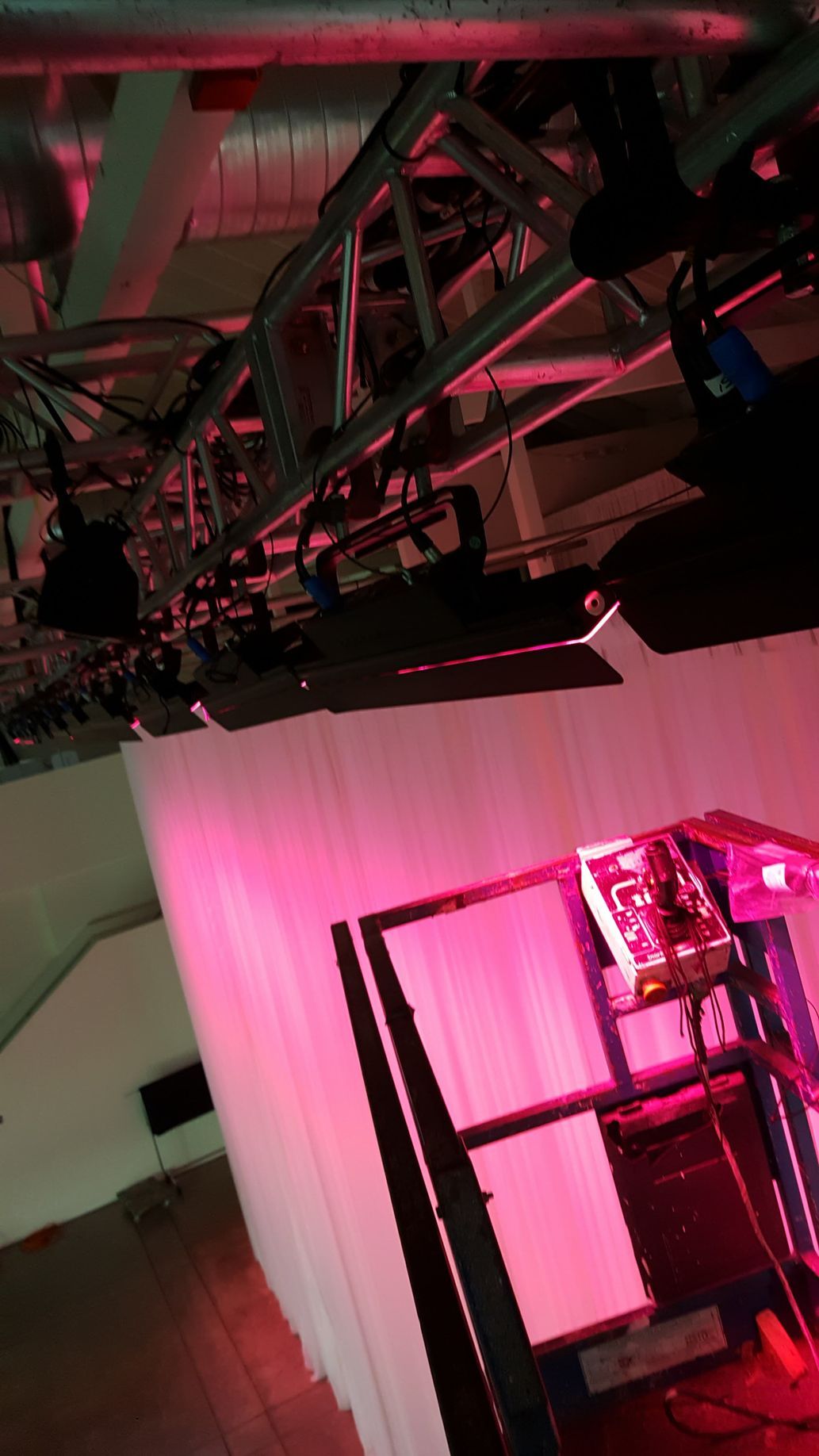 Red-lit stage setup with trussing, lights, and a white curtain. A lift is in the foreground.