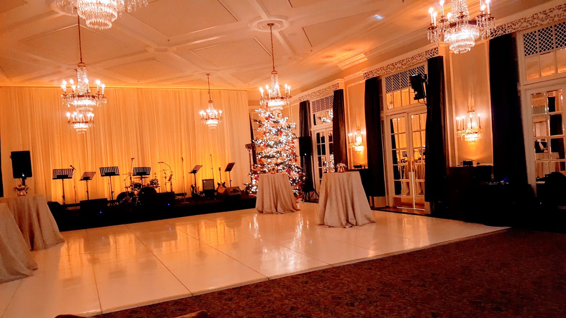 Elegant ballroom with white dance floor, chandeliers, and stage set for a performance.