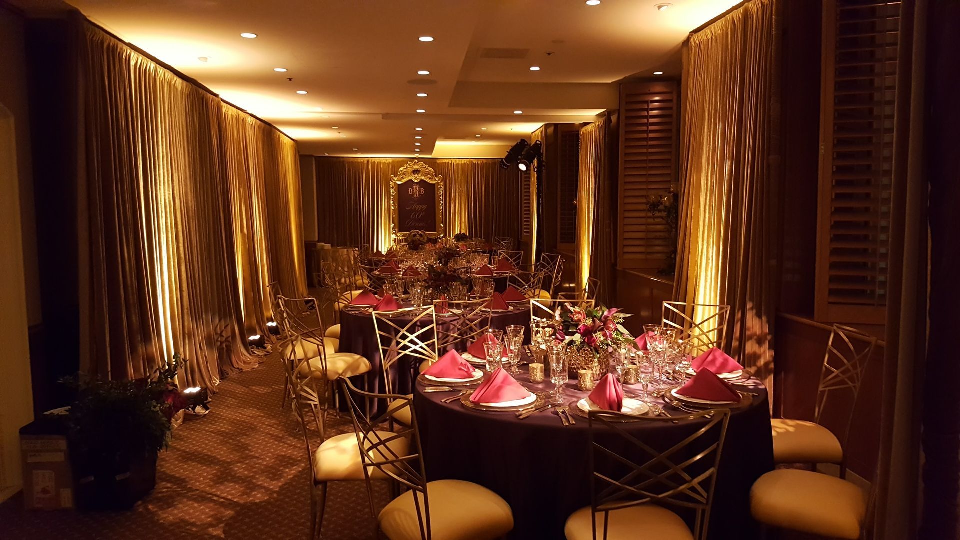 Formal dining room with round tables set for a banquet; gold chairs and table accents, red napkins.