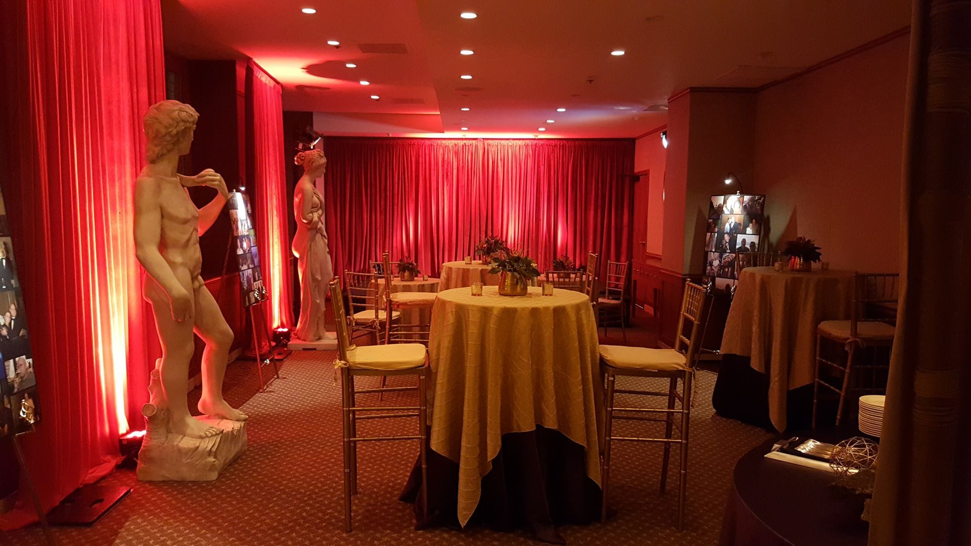 A dimly lit room with statues, tables, and red curtains; interior decor for an event.
