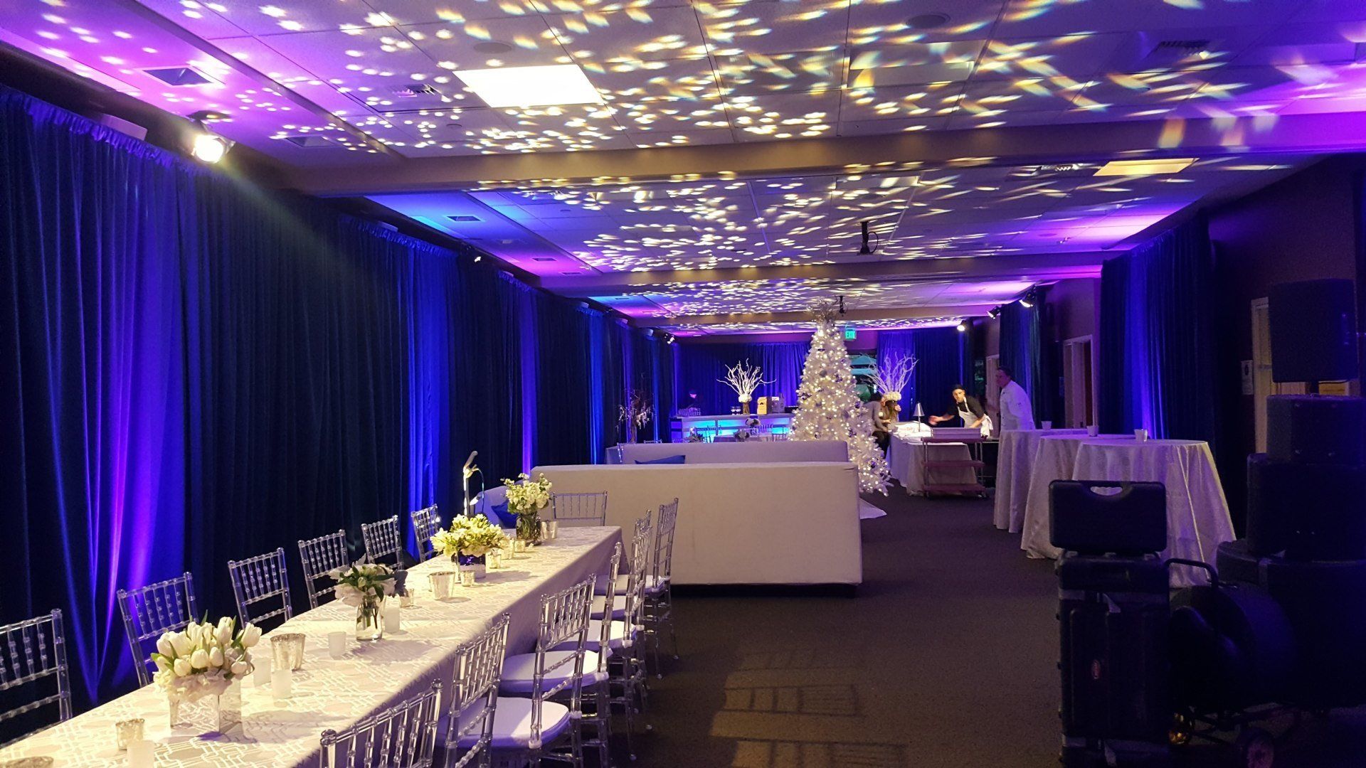 Event space with long tables, white decor, and blue and purple lighting.