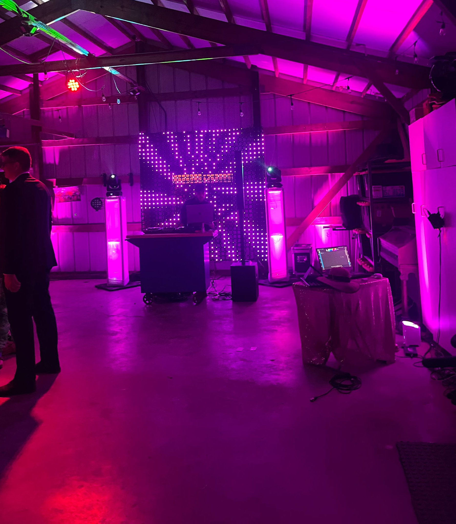 DJ setup in a dimly lit venue with pink and purple lighting. A person is DJing.