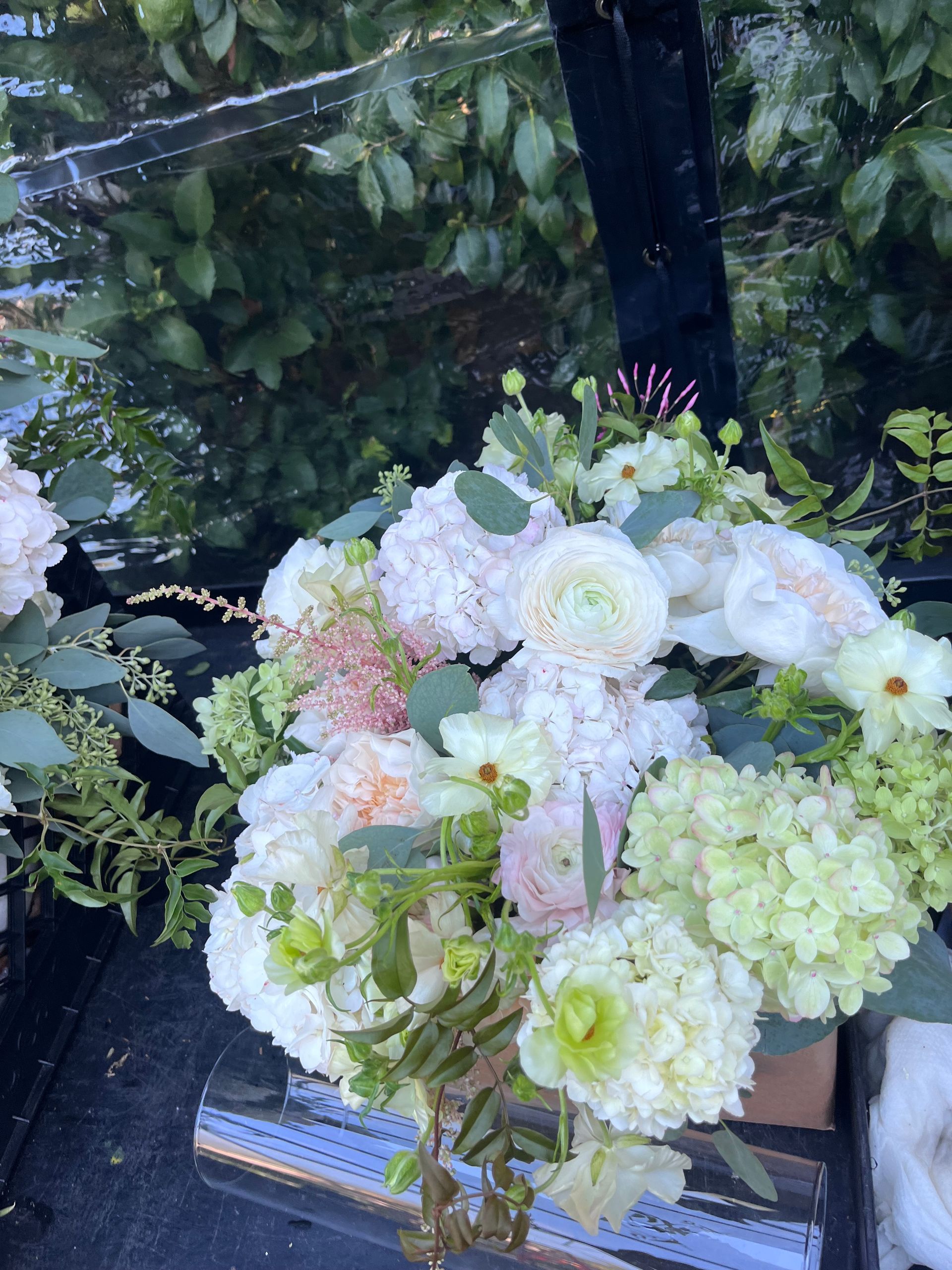 Close-up of a bouquet with white, green, and pink flowers in a glass vase; outdoors.
