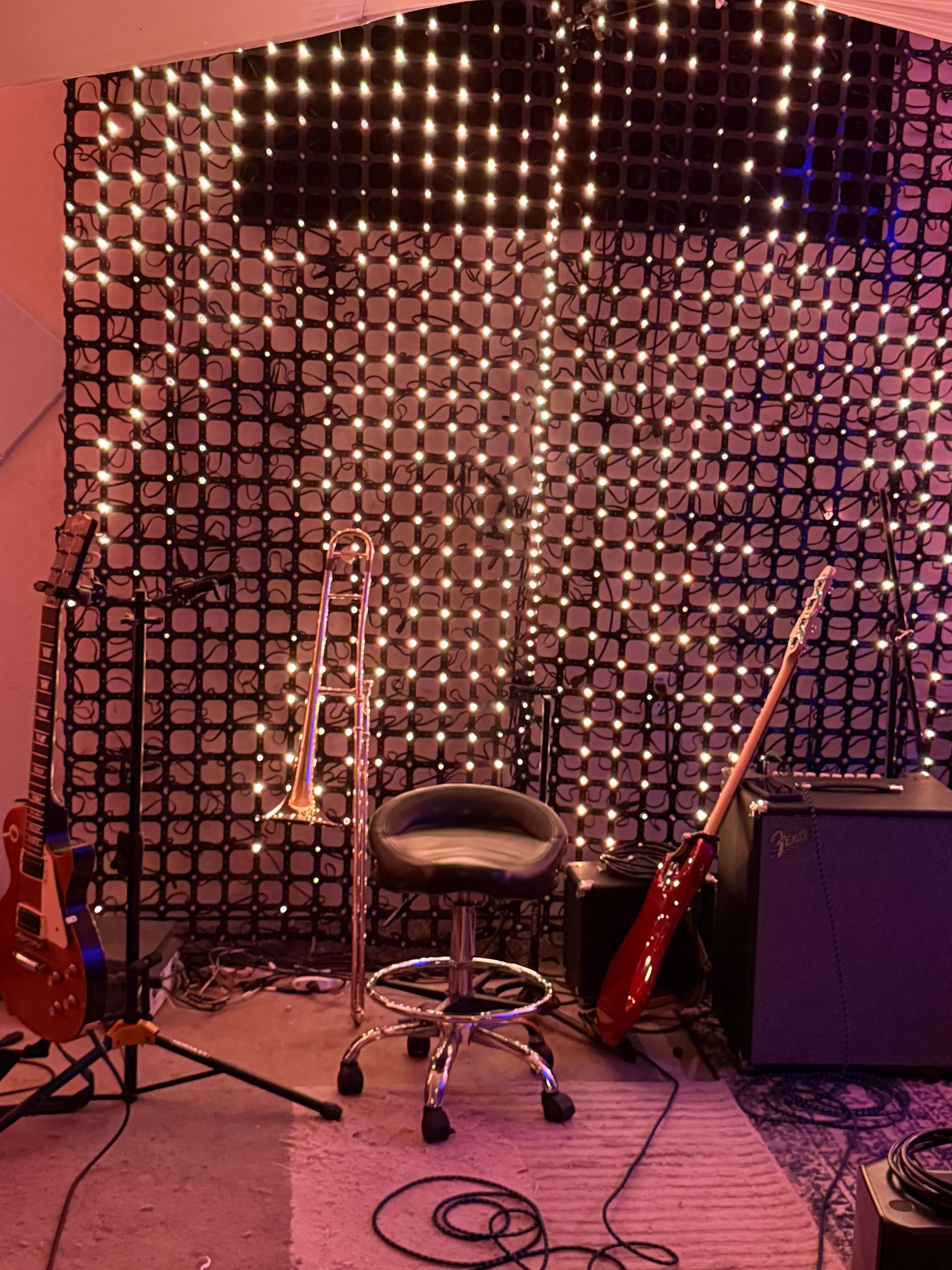 A music studio setup with a trombone, guitars, stool, and a backdrop of illuminated squares.