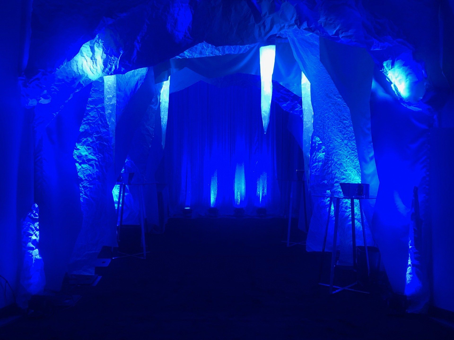 Blue-lit tunnel, decorated with white fabric and icicle-like structures, creating a cold, ice-themed atmosphere.