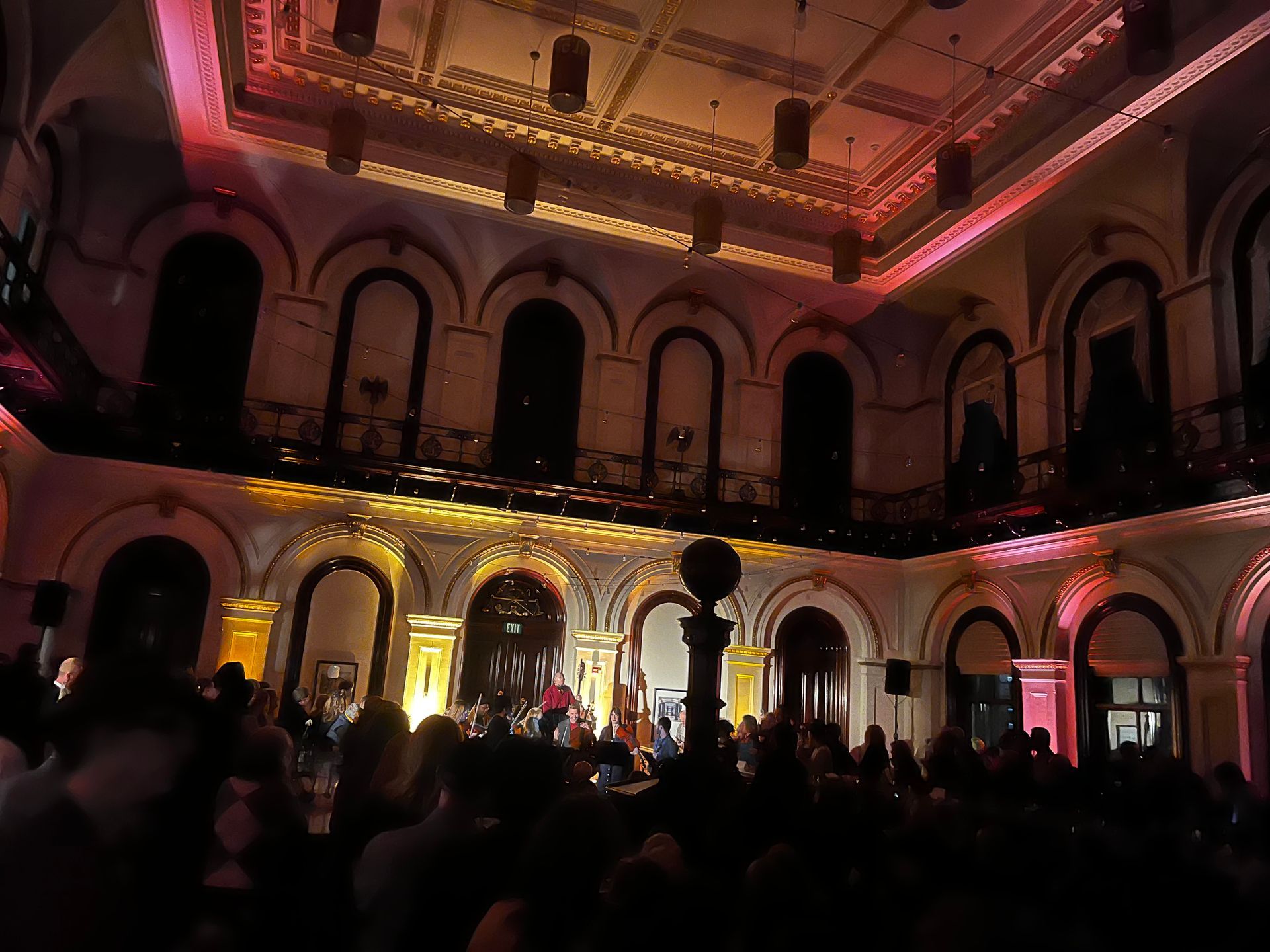 People at an event with band on stage in a large ornate building with colorful lighting.
