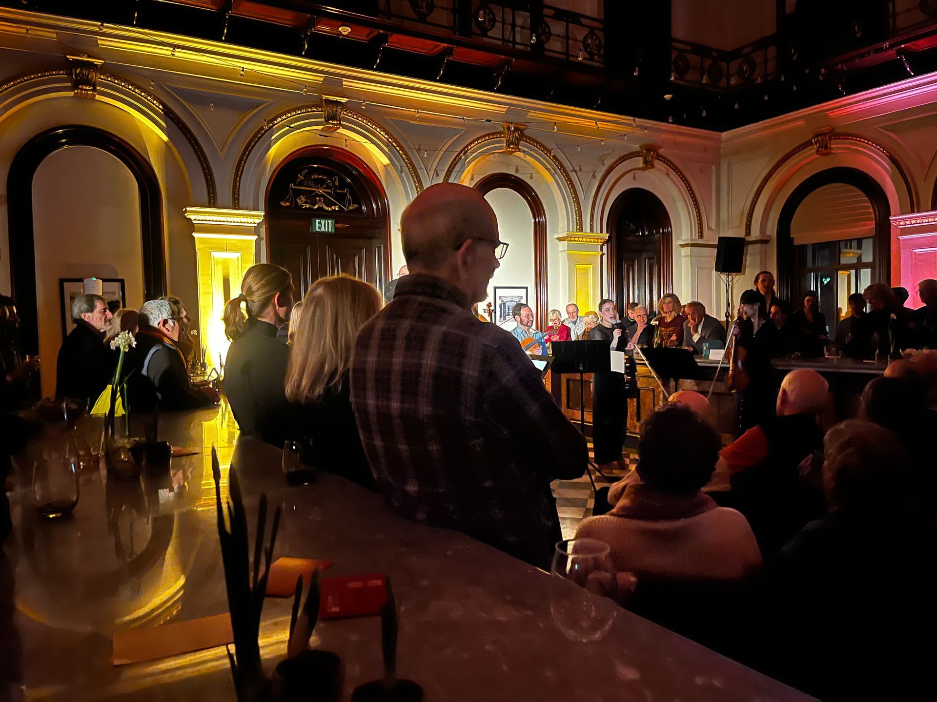 People watching a band perform in a historic building with arched doorways, ornate ceilings, and warm lighting.