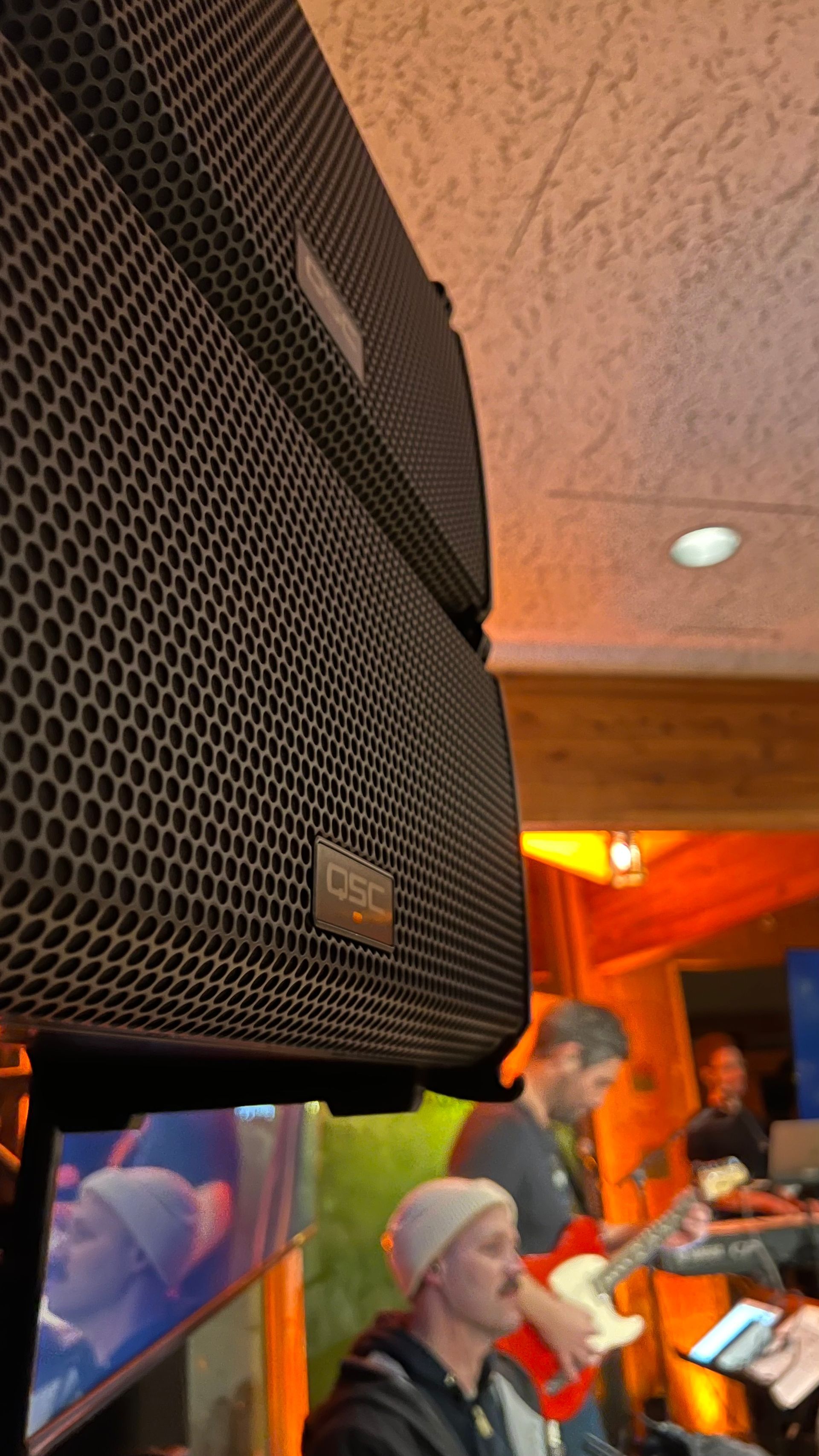 Black speaker stack over a band playing live music on stage.