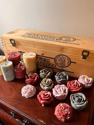 Candles in various colors and rose shapes on a wooden table, with a wooden box in the background.