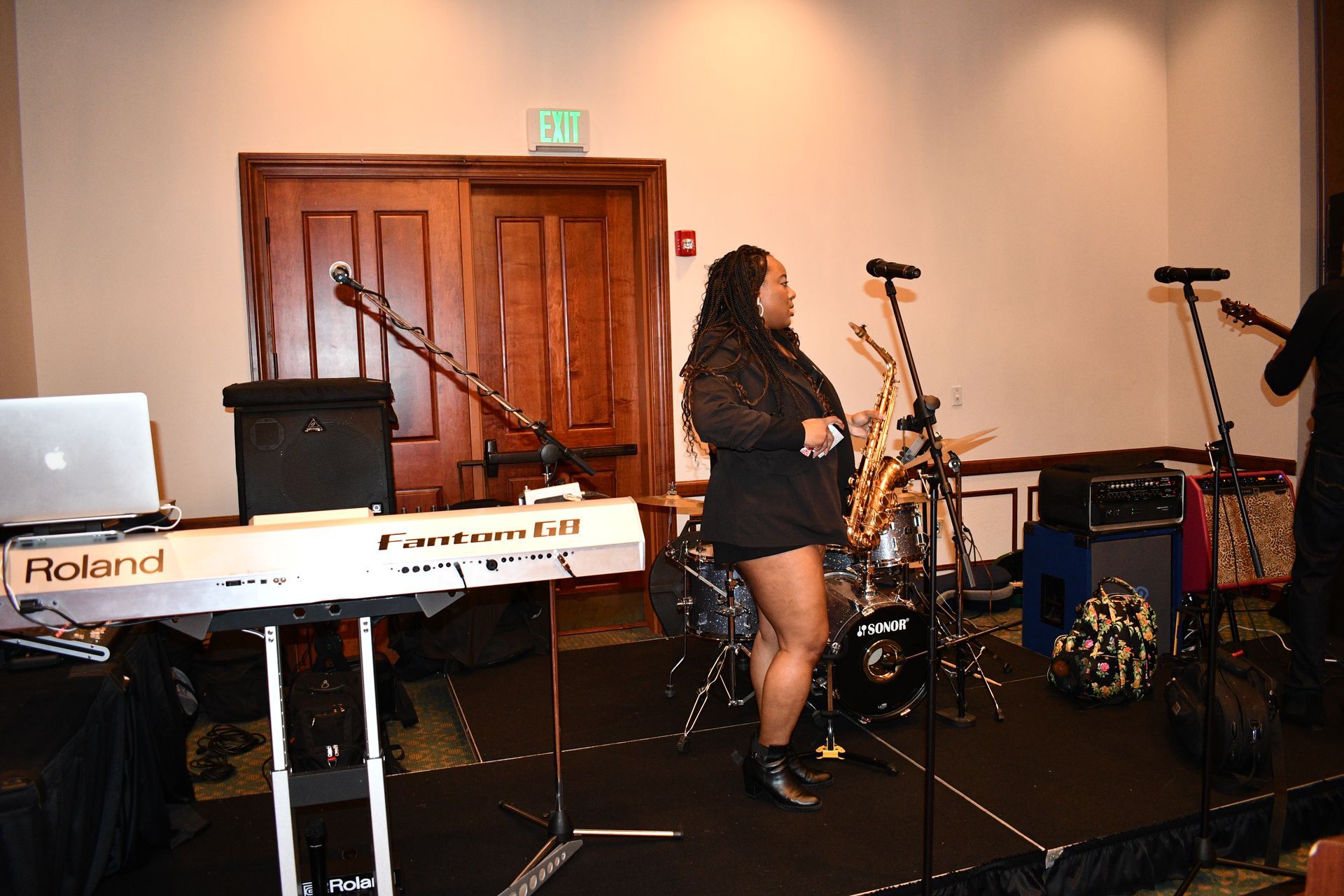 Band performing on stage: woman singing, keyboard, drums, saxophone, and guitarist.