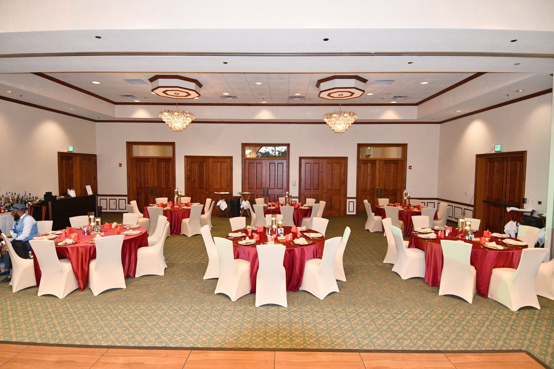 Banquet hall set for event with round tables draped in red, white chairs, and elegant chandeliers.
