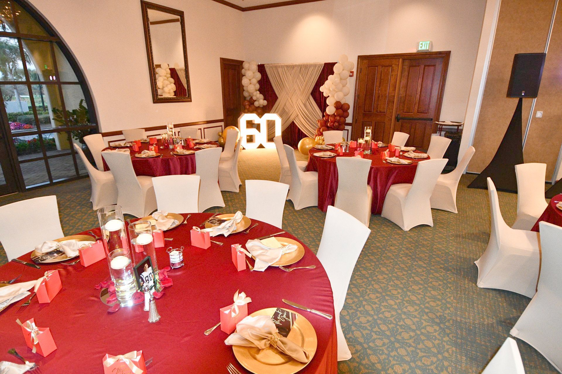 Party room set for a 60th birthday celebration. Round tables with red tablecloths, white chairs.