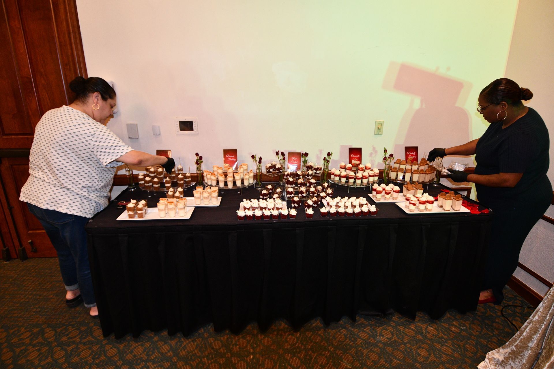 Two people arranging desserts on a table covered with a black cloth.