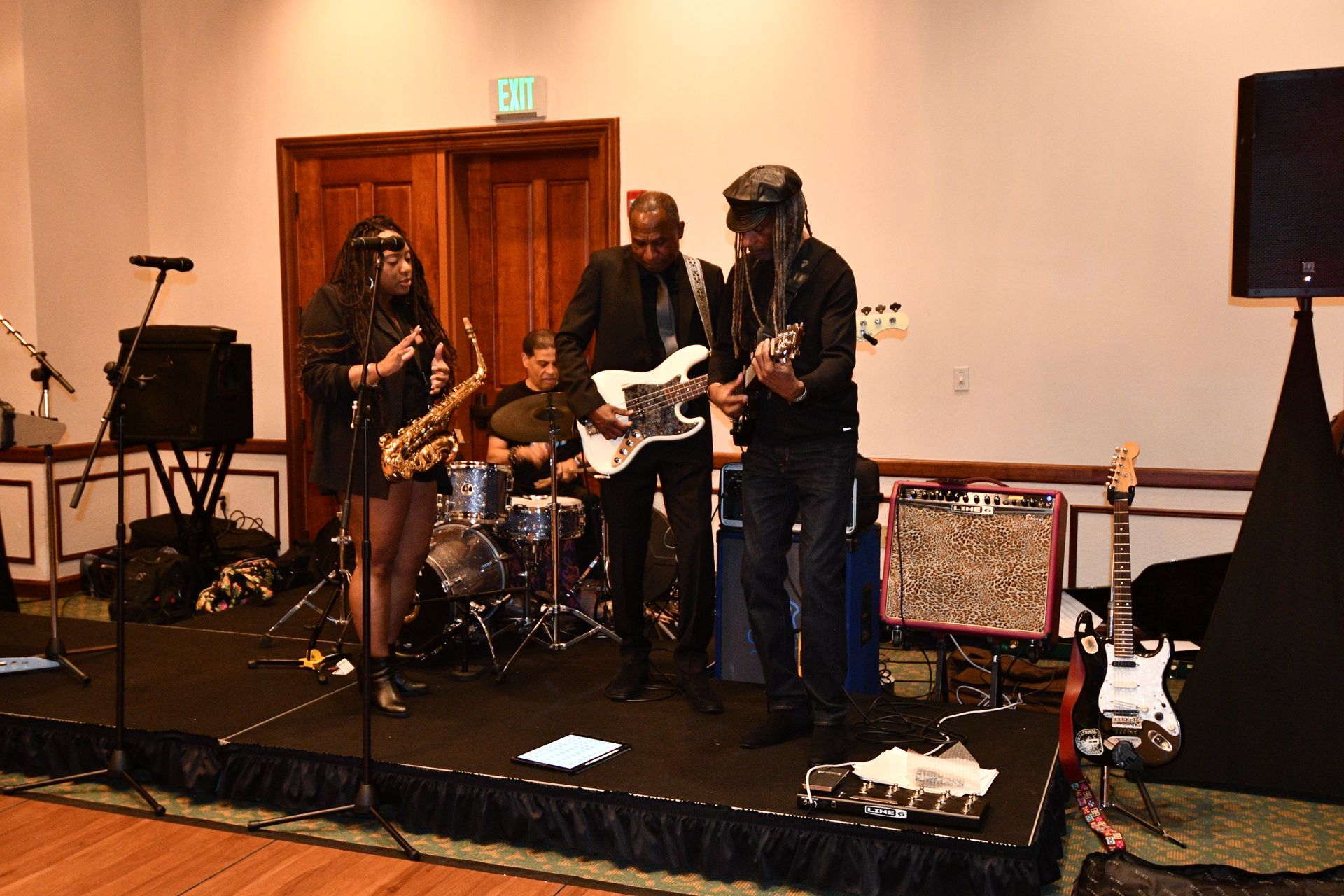 Band performing on stage: Saxophone player, bassist, guitarist, and drummer play in a venue with dark decor.