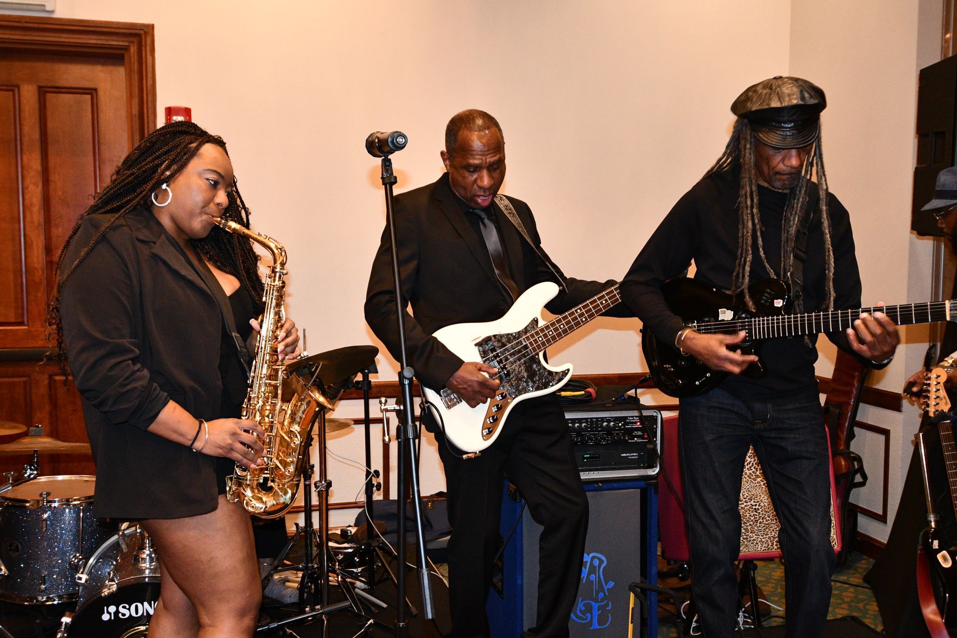 A band of three musicians performing live. A saxophonist, guitarist, and another guitarist play at an event.