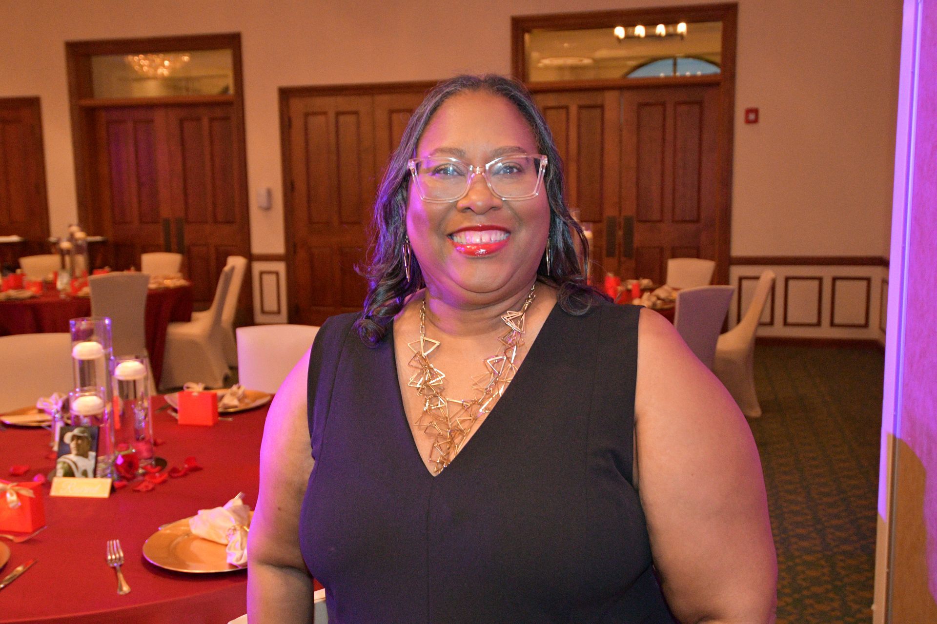 Woman in black dress smiles, standing near a red table in a decorated room.