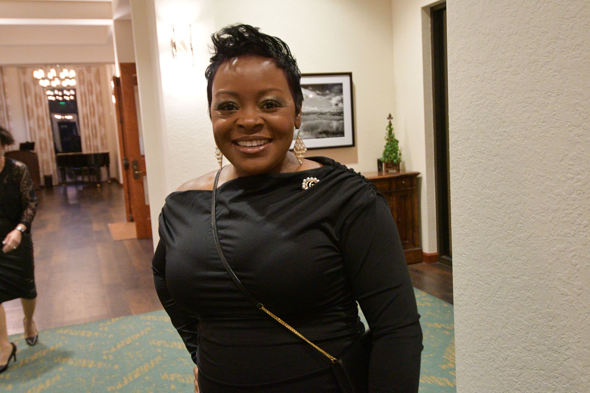Woman in black dress smiles indoors.