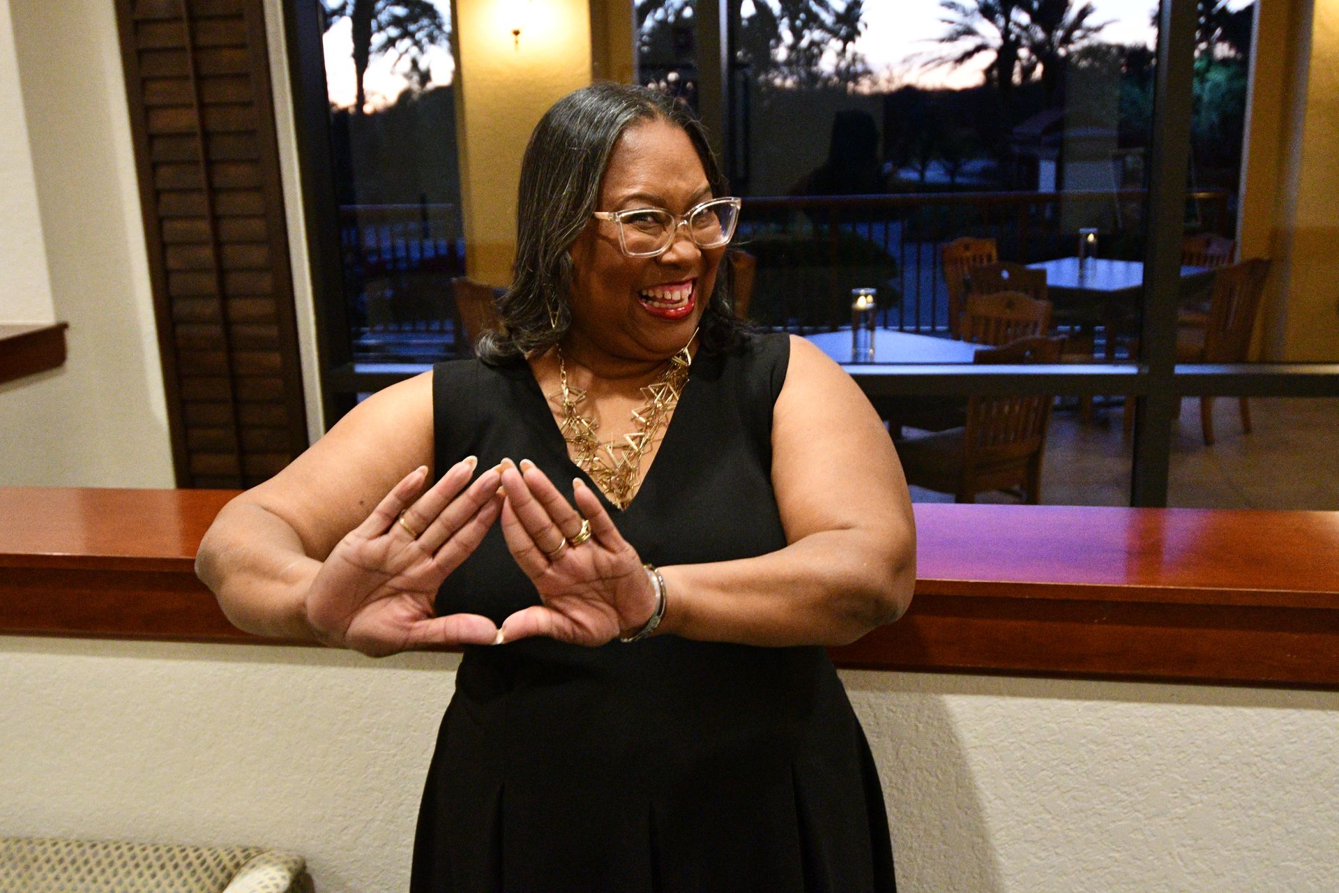 Woman in black dress, wearing glasses, forming a triangle with her hands.